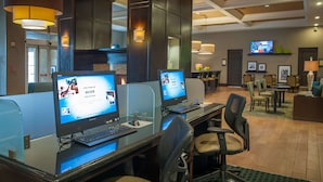 A hotel lobby with computer workstations, seating areas, and a television on the wall.