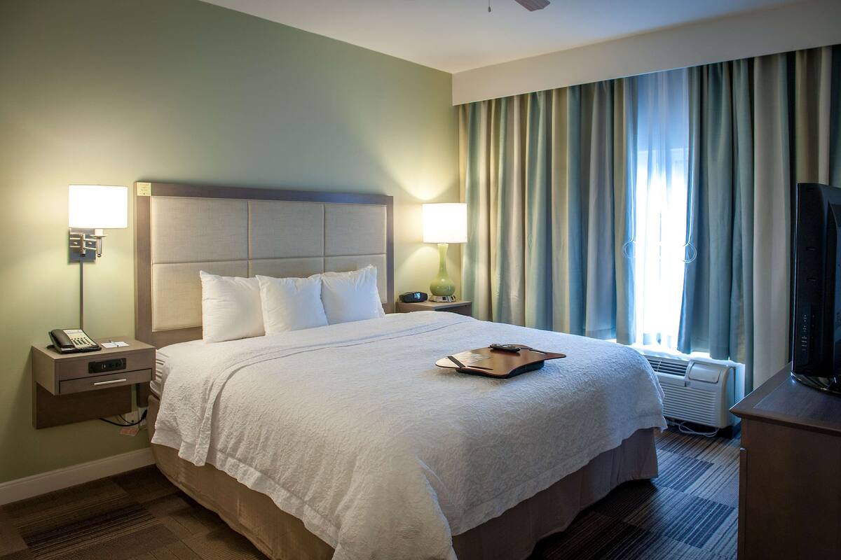 A hotel room with a large bed, two bedside lamps, a nightstand with a phone, and a television on a wooden stand.