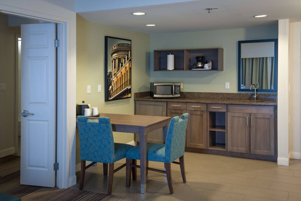 A modern kitchen with a dining area, featuring a microwave, cabinets, and a painting on the wall.