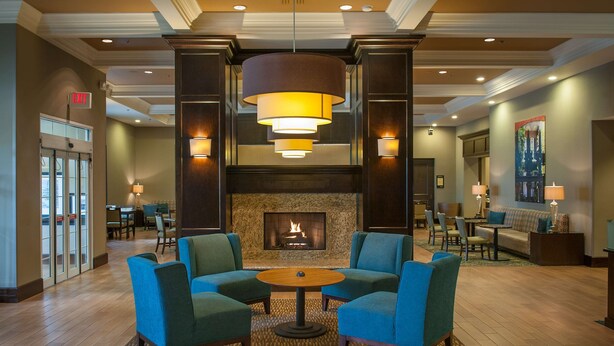 A lobby with a fireplace, blue armchairs, a round table, and a chandelier.
