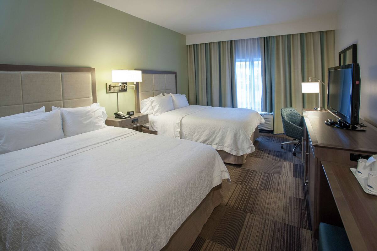 A hotel room with two beds, a desk with a television, and a chair.