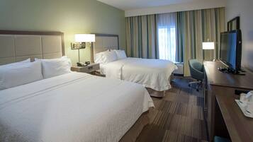 A hotel room with two beds, a desk with a television, and a chair.