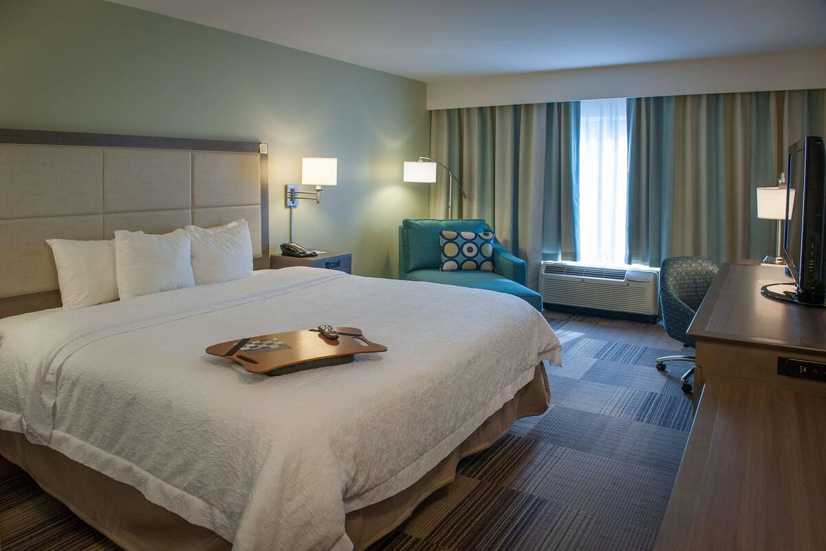 A hotel room with a large bed, a desk, a chair, a TV, and a window with curtains.