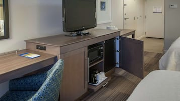 Ett hotellrum med en säng, en TV, ett skrivbord med en stol, en mikrovågsugn och en kaffebryggare.