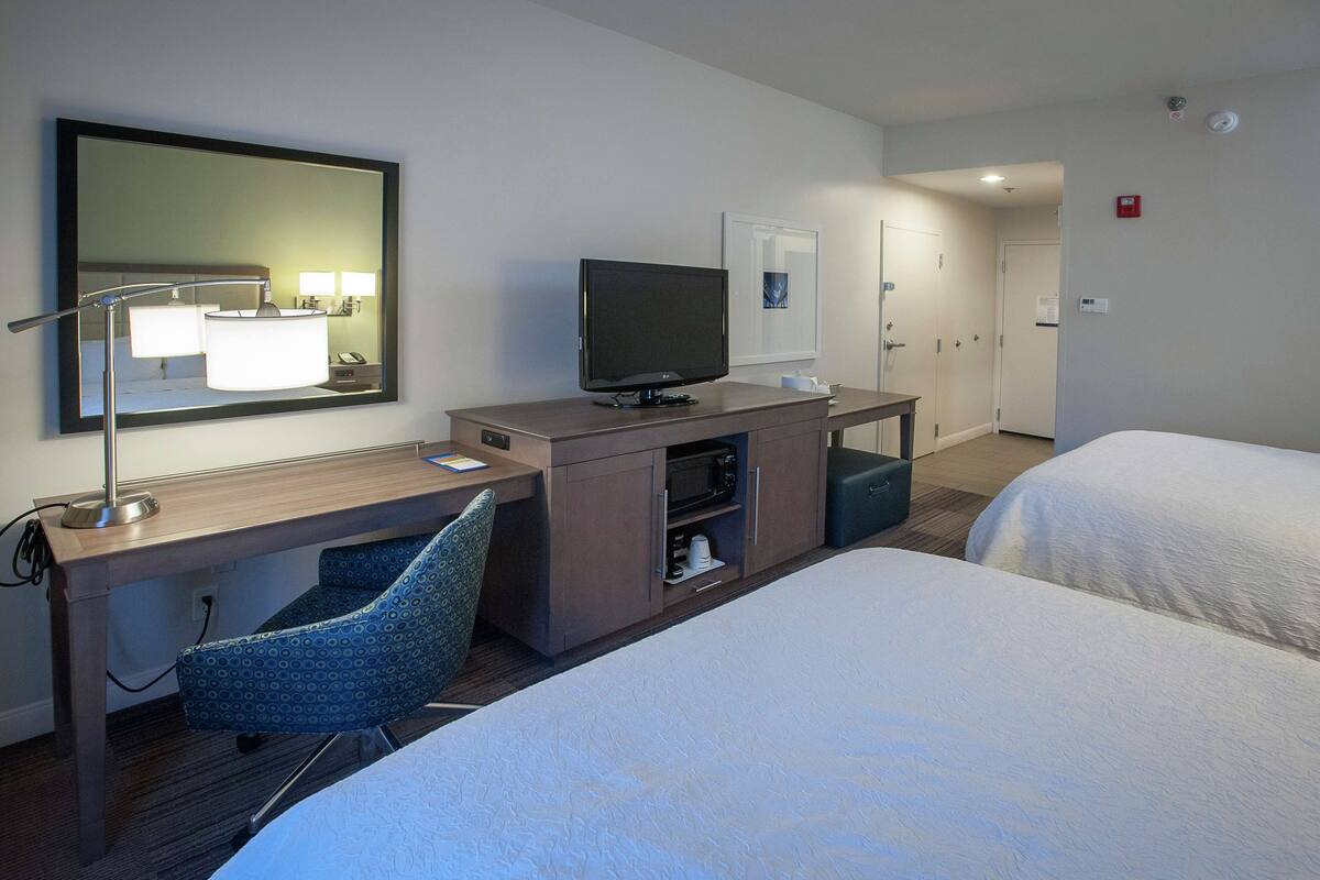 A hotel room with a desk, chair, television, and two beds.