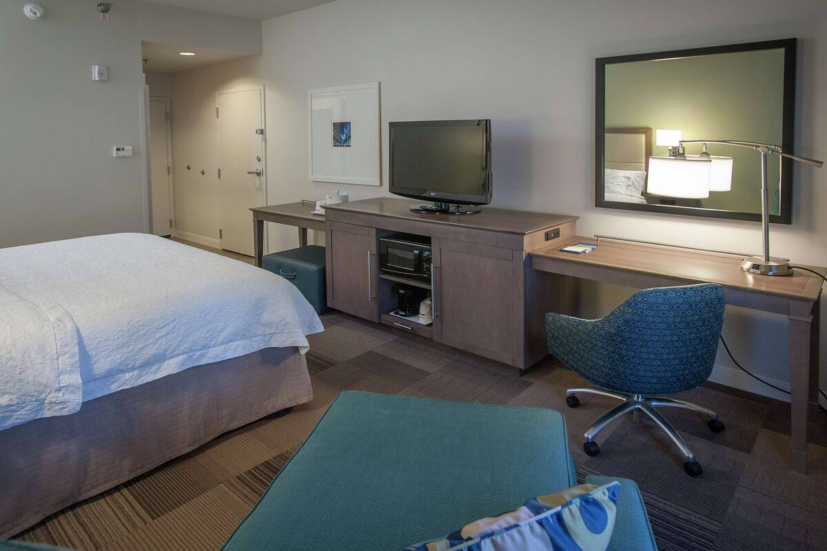 A hotel room with a bed, desk, chair, TV, and a mirror.