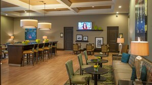 A hotel lobby with a bar area, seating arrangements, and a television screen.