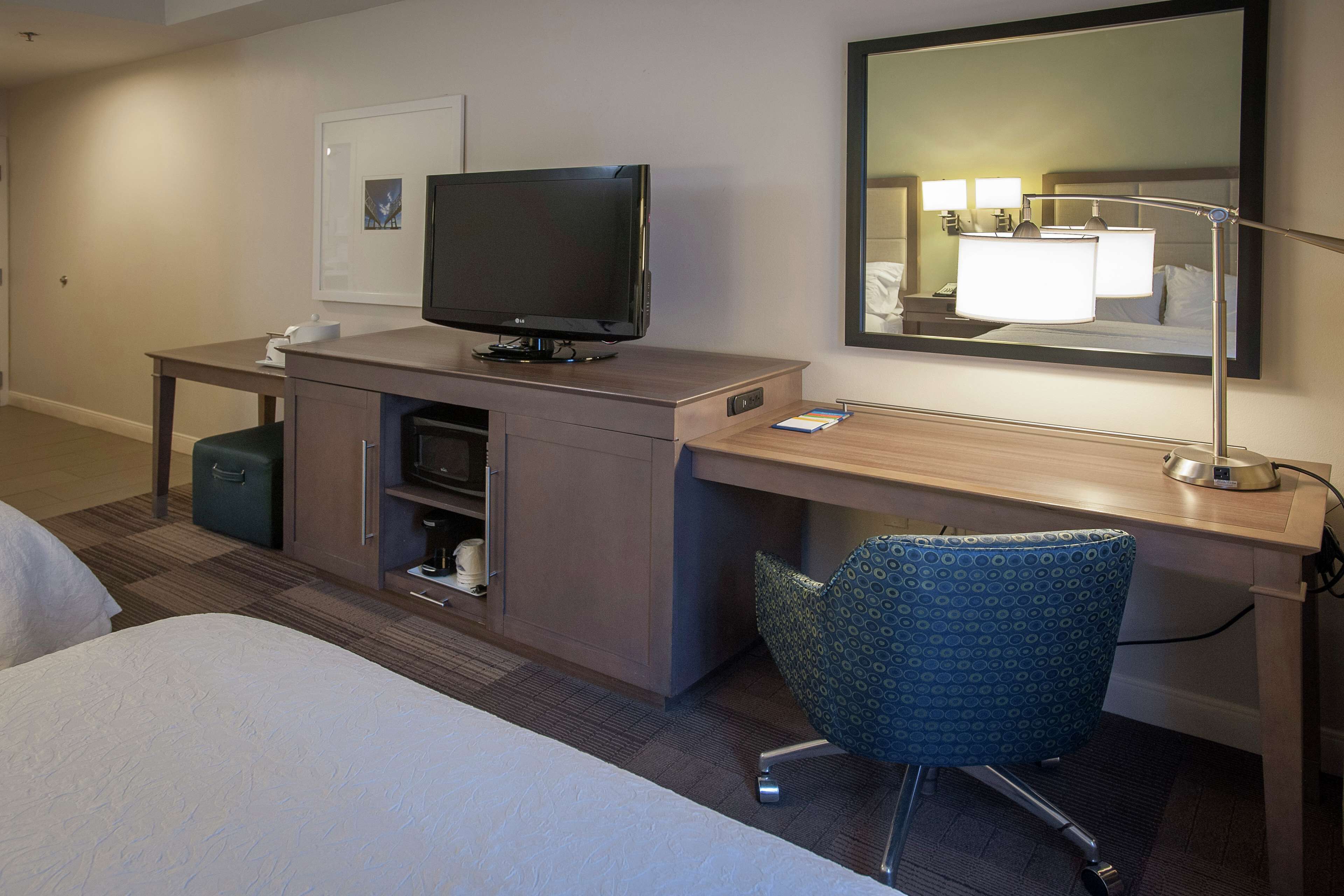 Une chambre d’hôtel comprenant un lit, un bureau avec un ordinateur, une télévision, une chaise et un miroir.