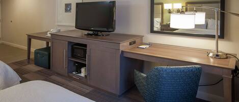 Une chambre d’hôtel comprenant un lit, un bureau avec un ordinateur, une télévision, une chaise et un miroir.