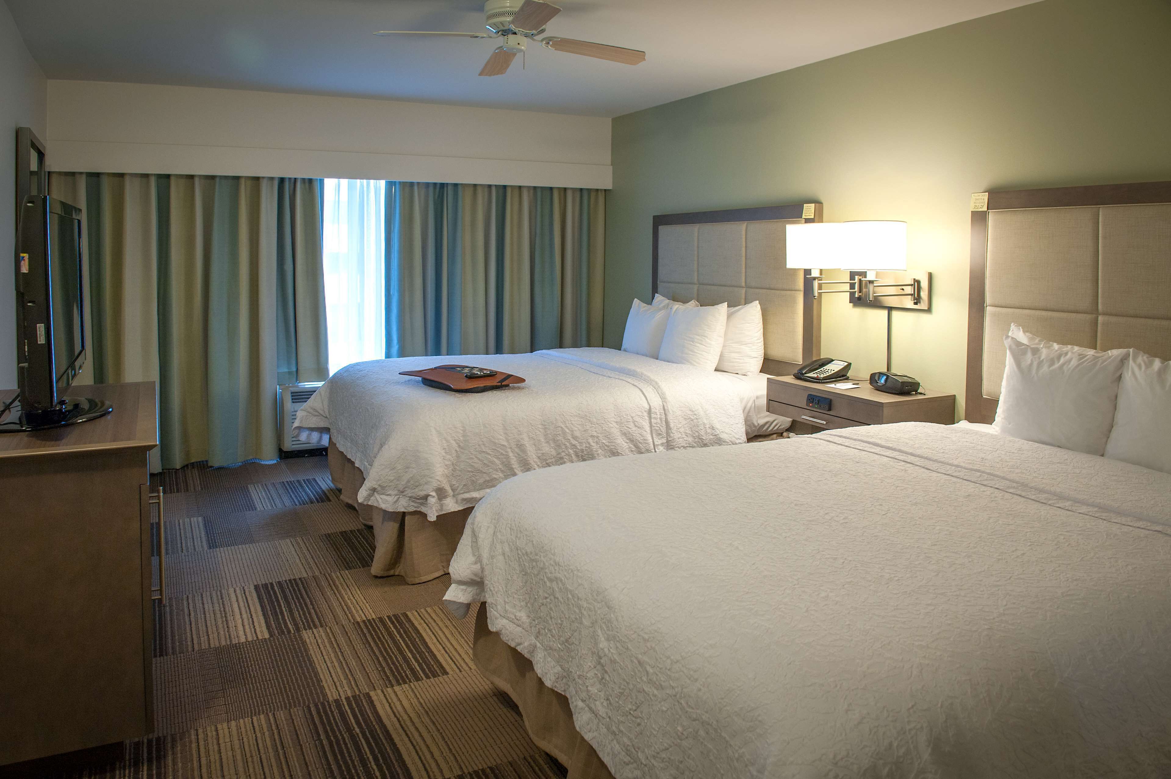 A hotel room with two beds, a desk with a telephone, and a ceiling fan.