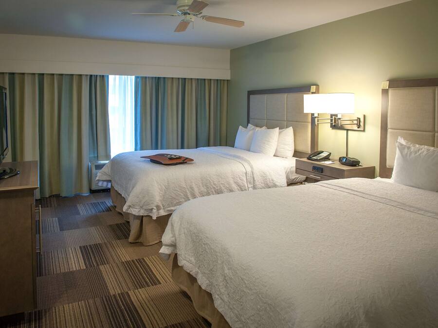 A hotel room with two beds, a desk with a telephone, and a ceiling fan.