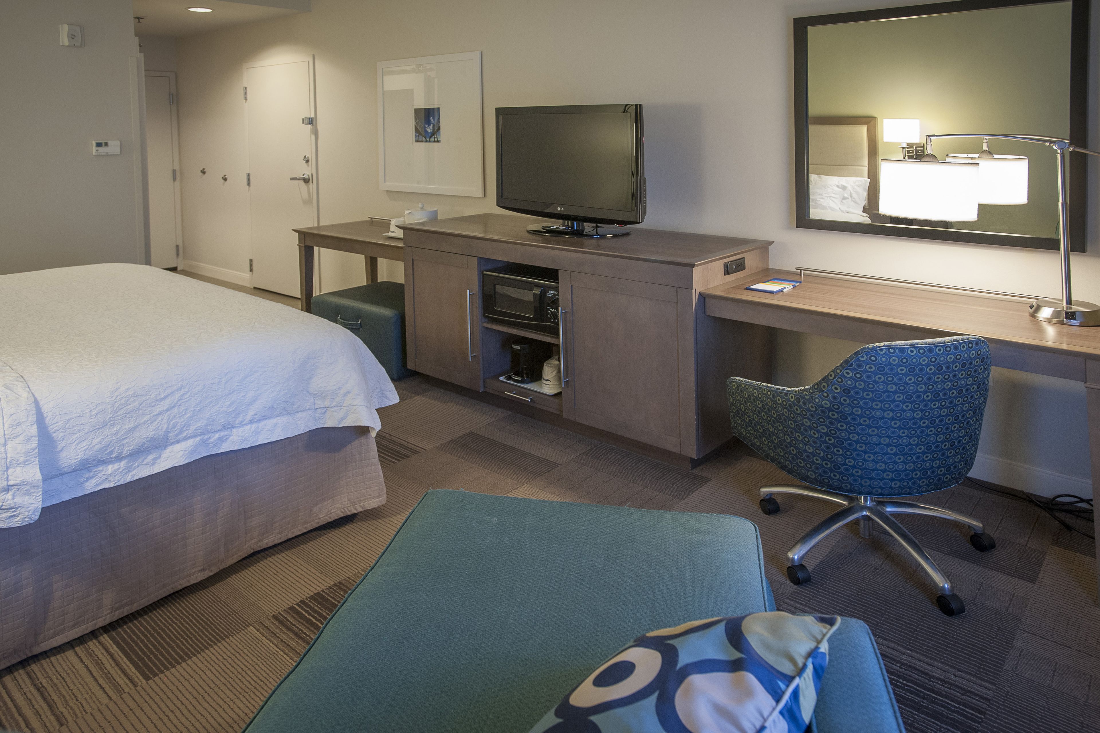 A hotel room with a bed, desk, chair, TV, and a mirror.