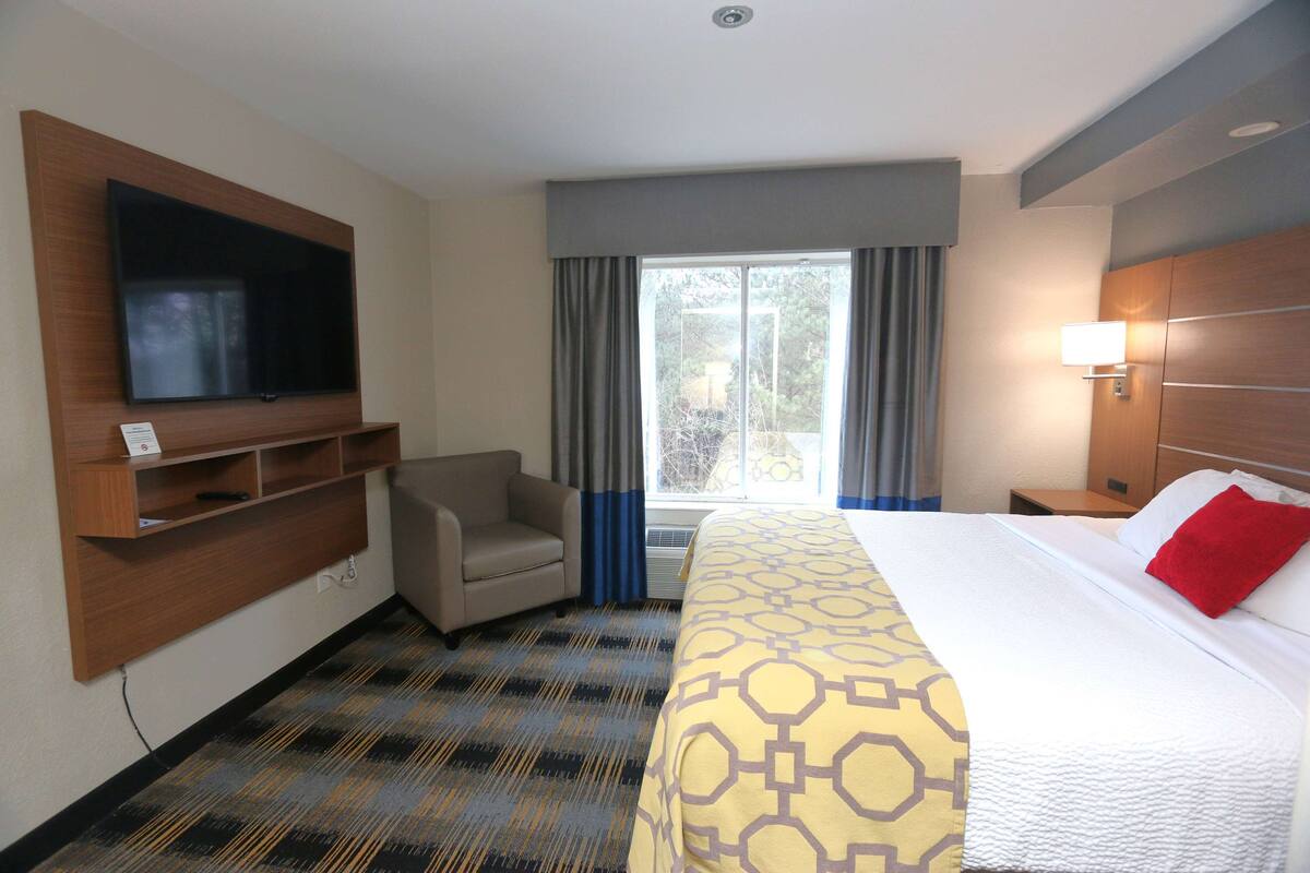 Habitación de hotel con cama, televisión montada en la pared, escritorio y silla.