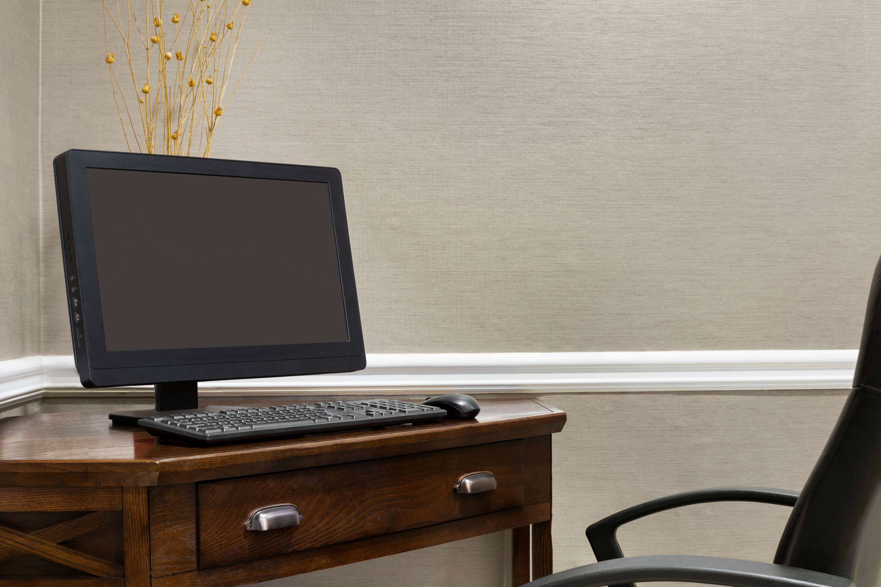 A wooden desk with a computer monitor, keyboard, and mouse.