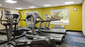 Ein Fitnessstudio mit Laufbändern und Crosstrainern, großen Fenstern und einer gelben Wand.