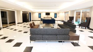 Eine geräumige Lobby mit einer grauen Couch, einem kleinen Tisch und einem Fernsehbildschirm.