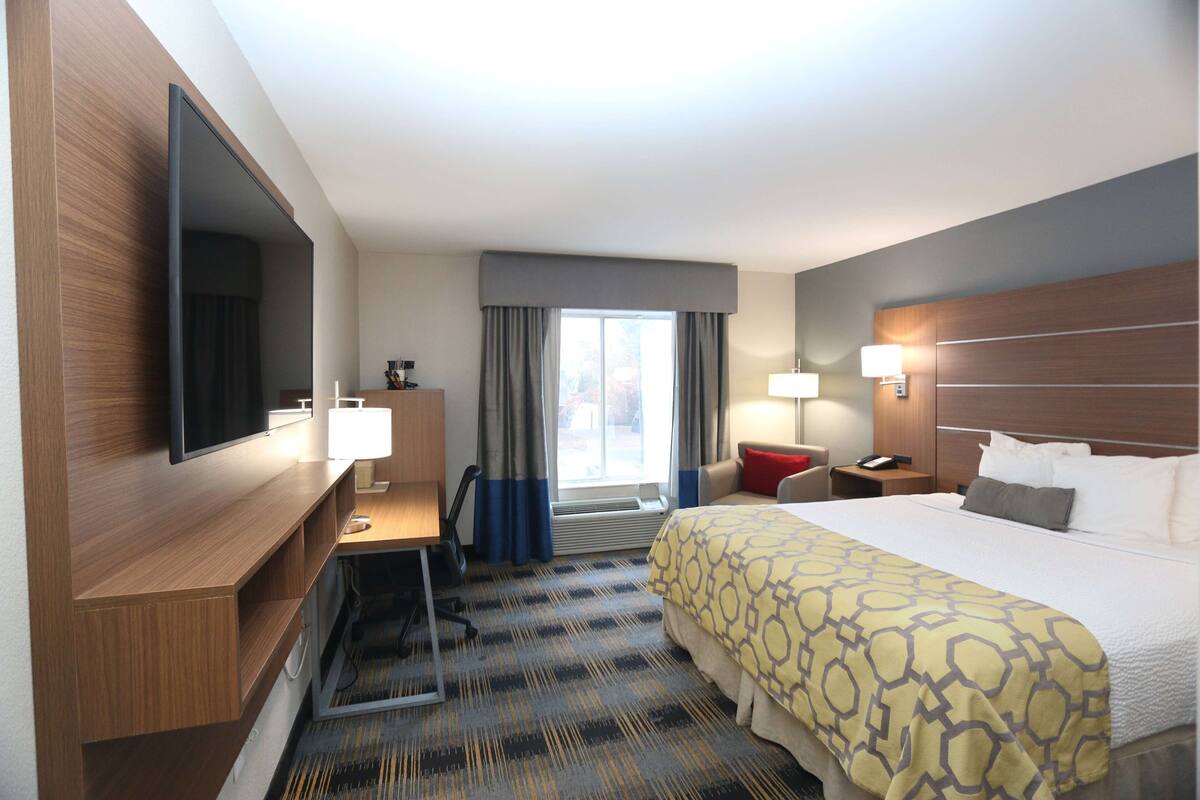 Habitación de hotel con una cama grande, un escritorio, un televisor de pantalla plana, una ventana con cortinas y una mesita de noche con lámpara.