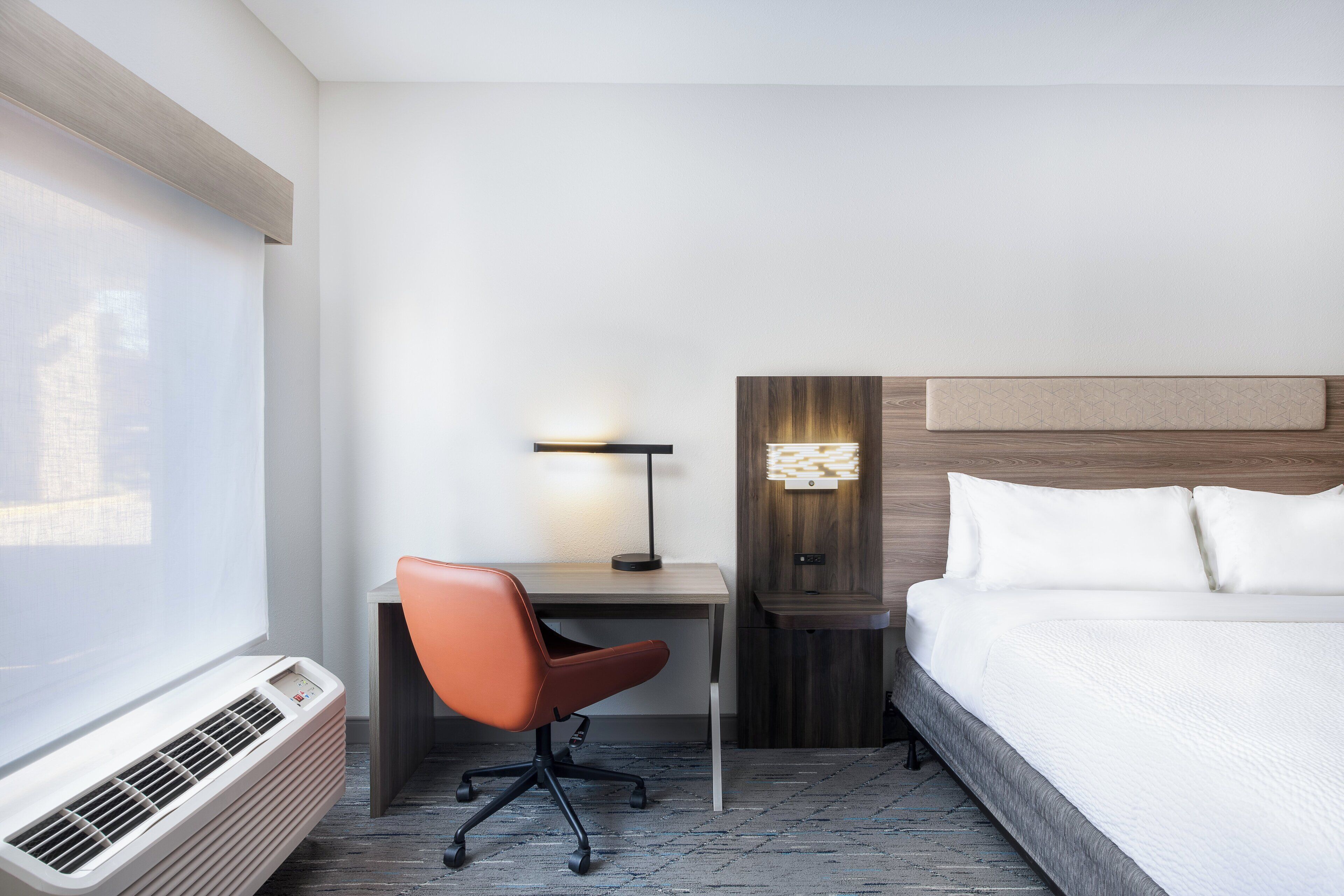Une chambre d’hôtel équipée d’un lit, d’un bureau, d’une chaise, d’une lampe et d’un appareil de climatisation.