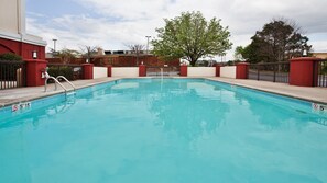 Enjoy a refreshing swim in the pool surrounded by lush greenery and a nearby building.