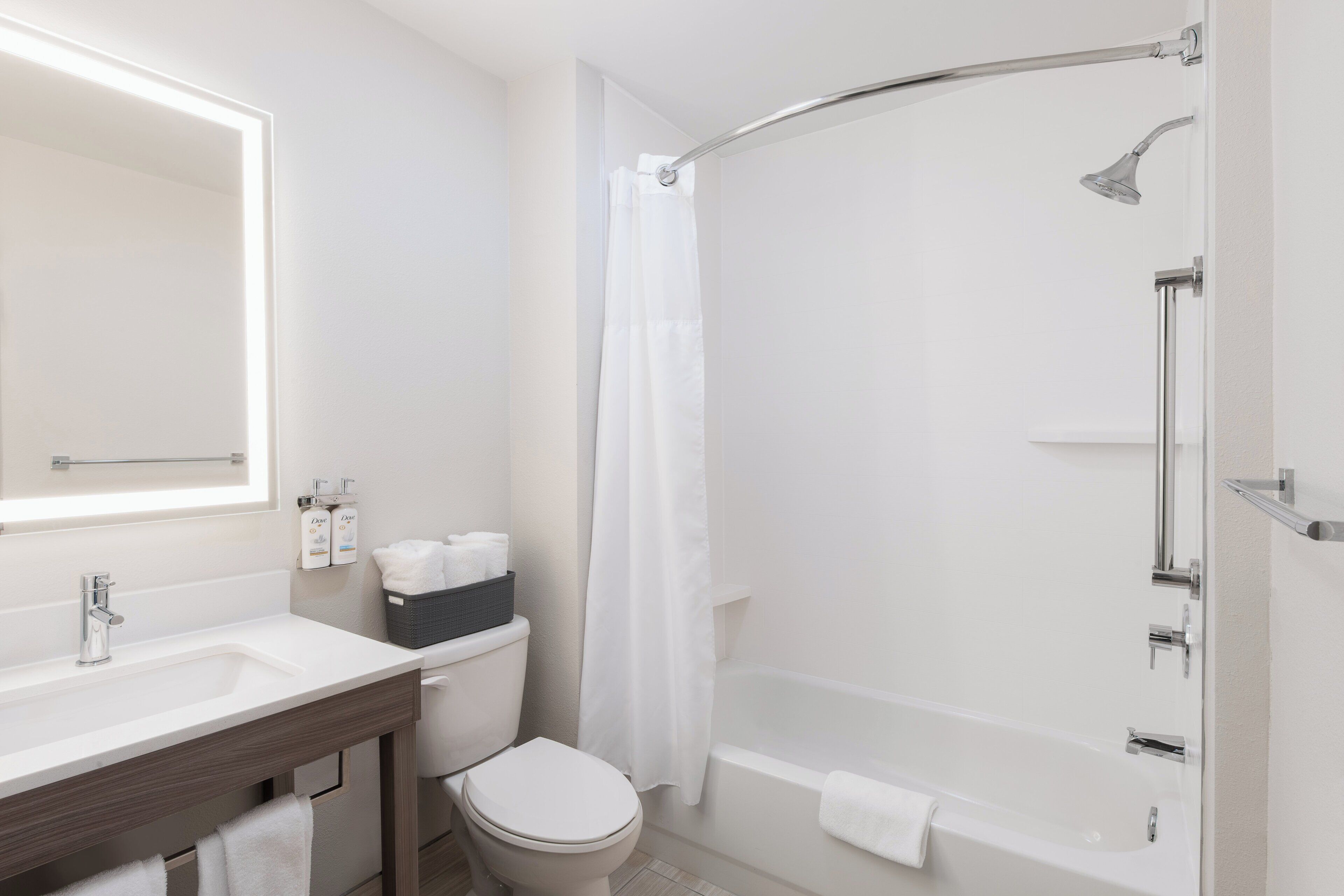 A modern bathroom with a white sink, a toilet, a shower with a curved glass door, and a large mirror.