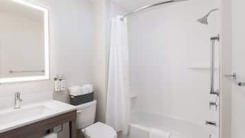 Un baño moderno con un lavamanos blanco, un inodoro, una ducha con puerta de vidrio curva y un espejo grande.