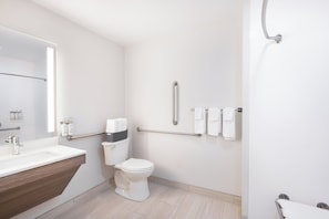Bathroom features a white sink, toilet, and handrail for accessibility, with towels neatly hung on the wall.