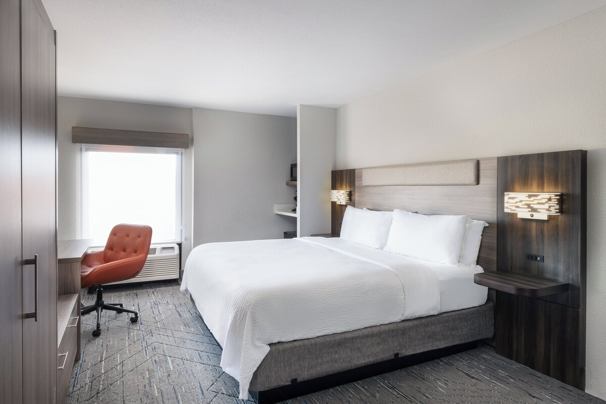 A hotel room with a large bed, a chair, a desk, and a window.