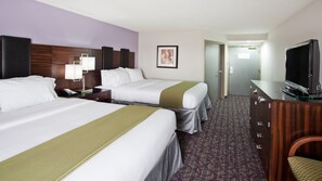 Two single beds with white linens and green throw pillows, a flat-screen TV, and a nightstand with a lamp.