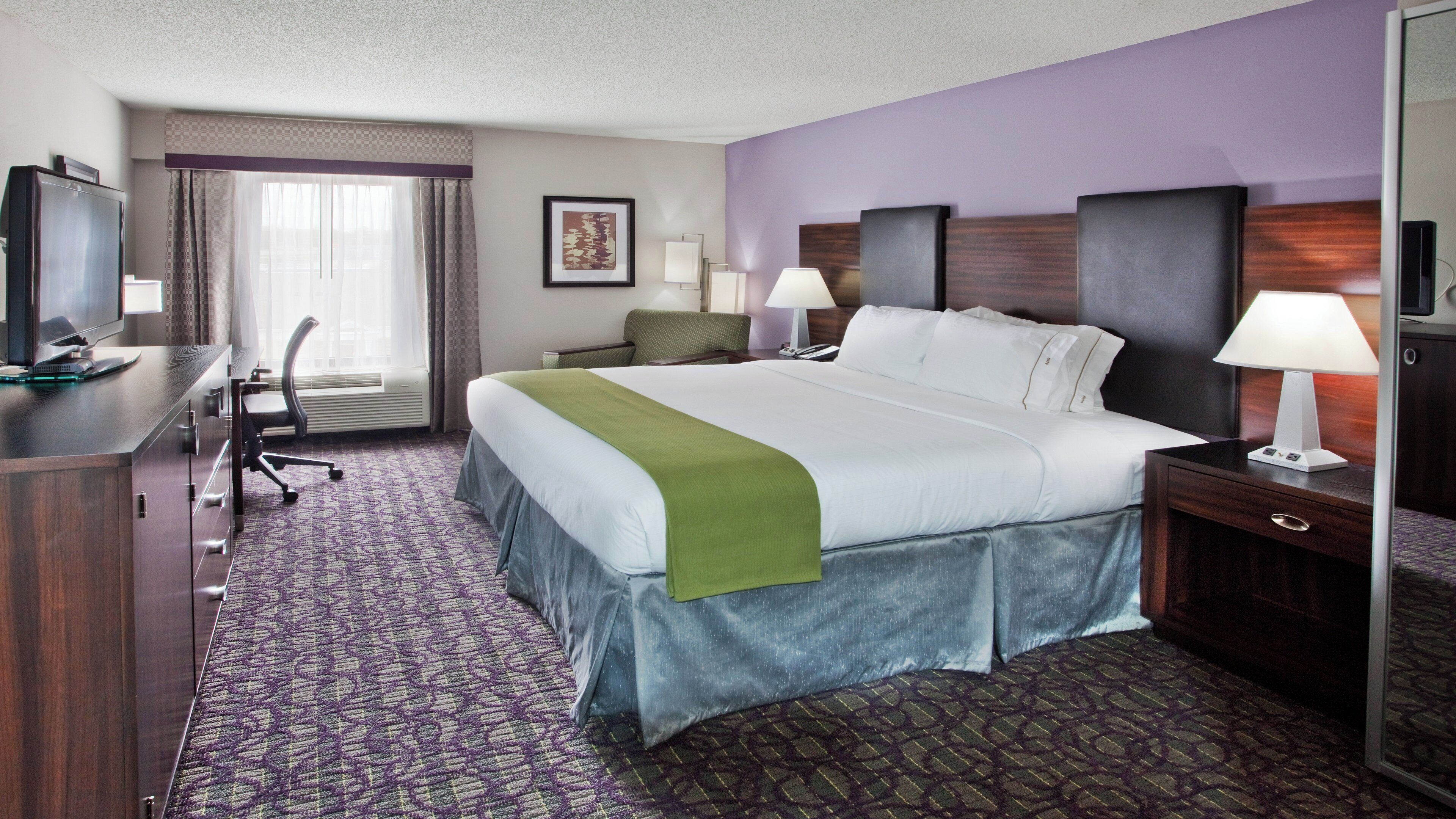 A hotel room with a bed, desk, chair, and a television.