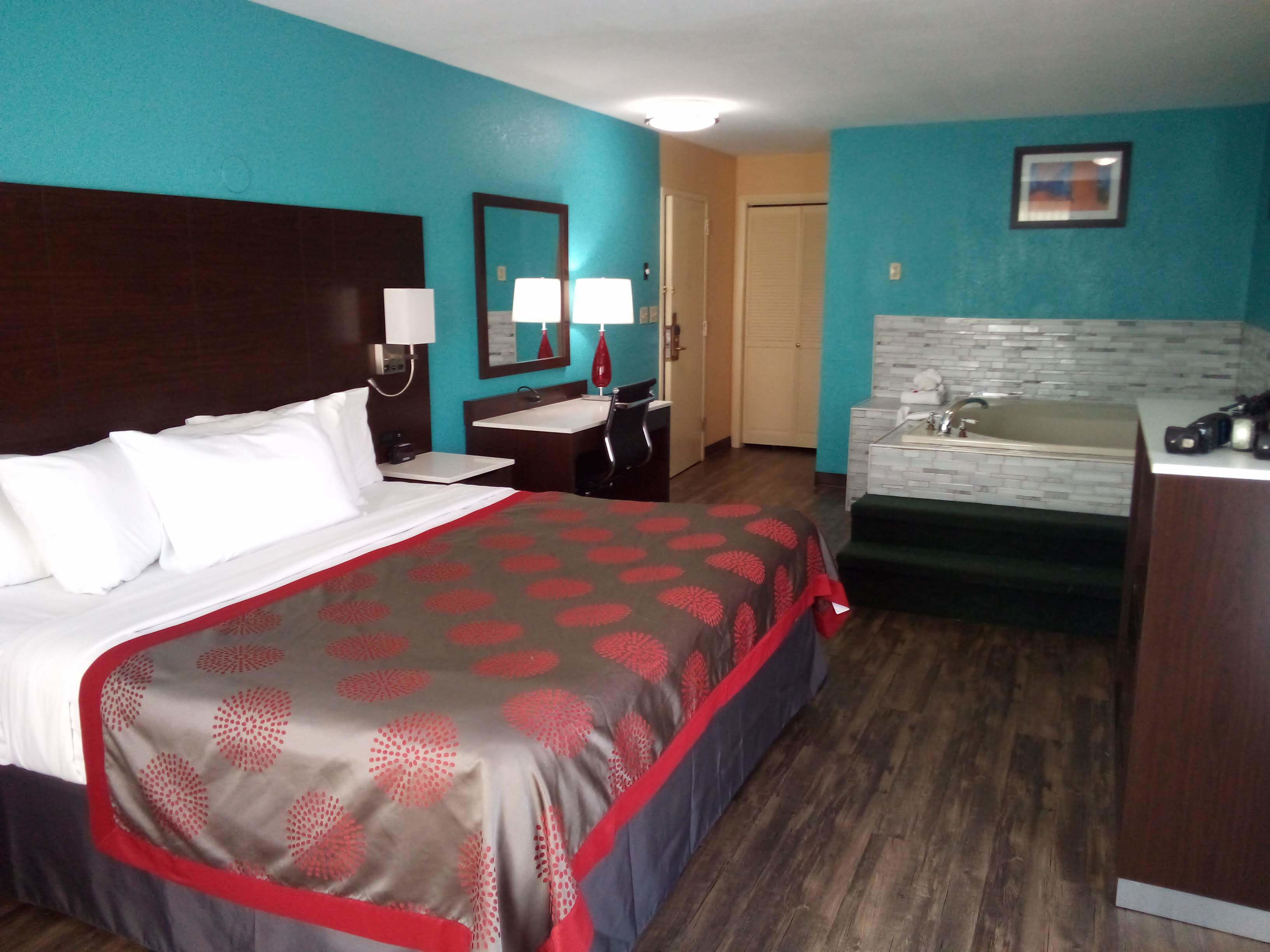 A hotel room with a bed, a desk, a chair, a mirror, a sink, and a door.
