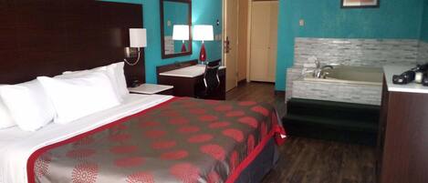 A hotel room with a bed, a desk, a chair, a mirror, a sink, and a door.
