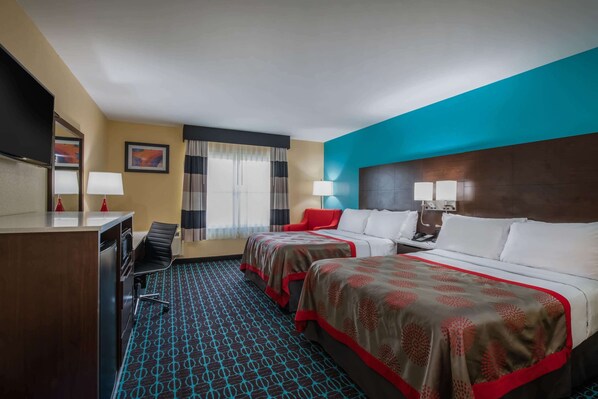 A hotel room with two beds, a desk, a chair, a TV, and a window with curtains.