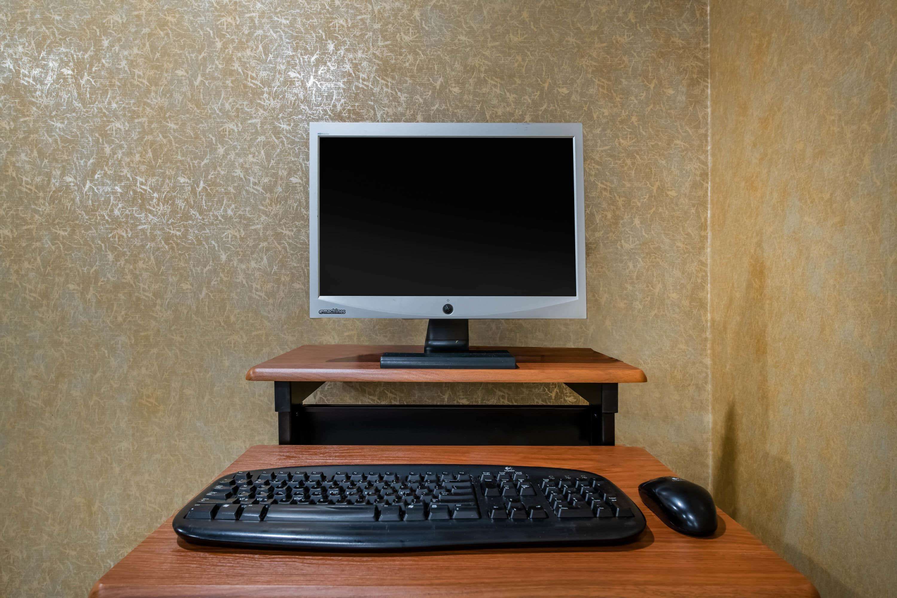 A computer setup with a monitor, keyboard, and mouse on a wooden desk against a textured wall.