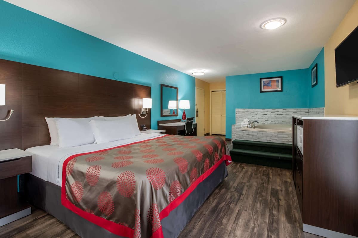 A hotel room with a large bed, a desk, a chair, a sink, and a mirror.