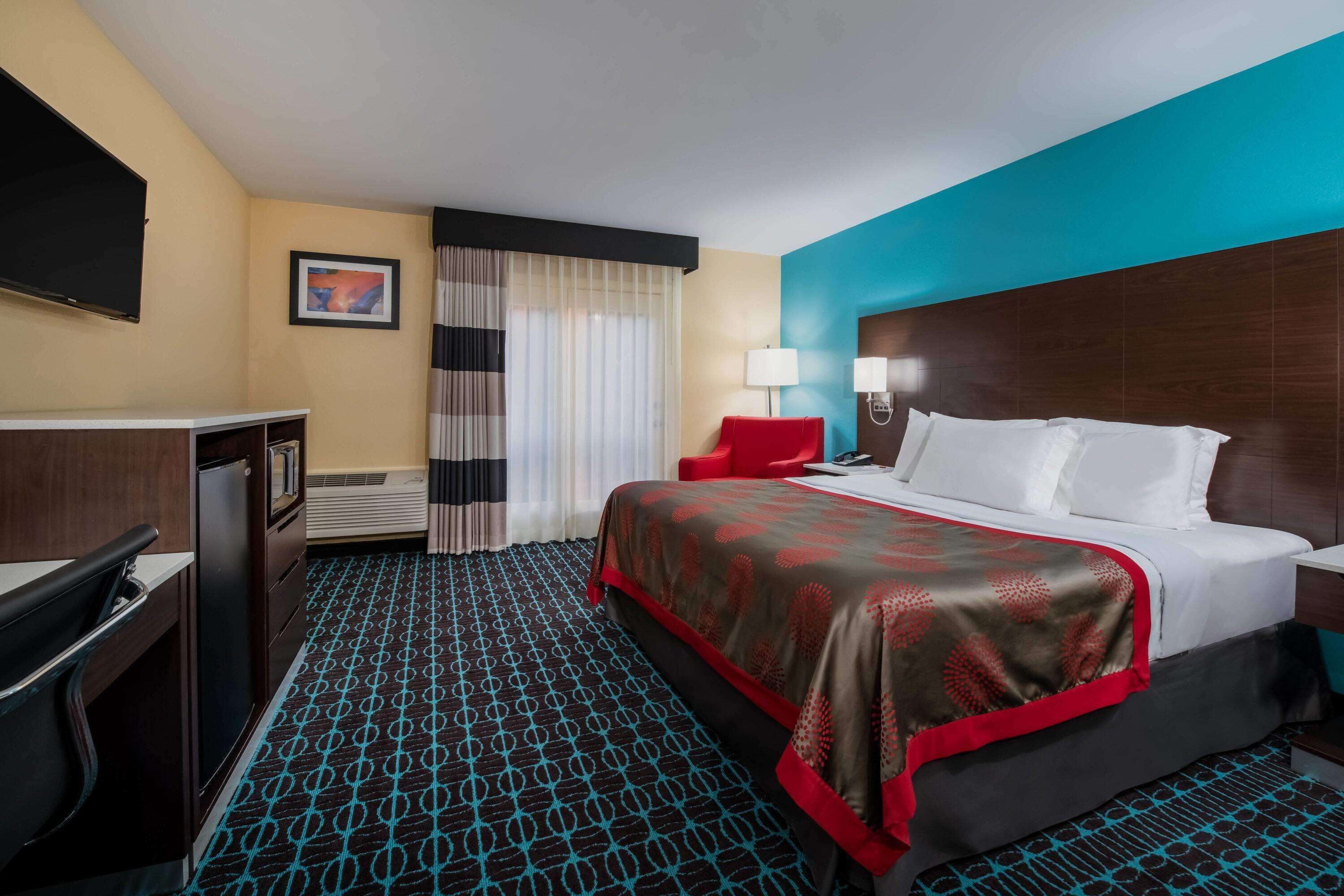 Habitación de hotel con cama, escritorio, silla, televisor y ventana con cortinas.