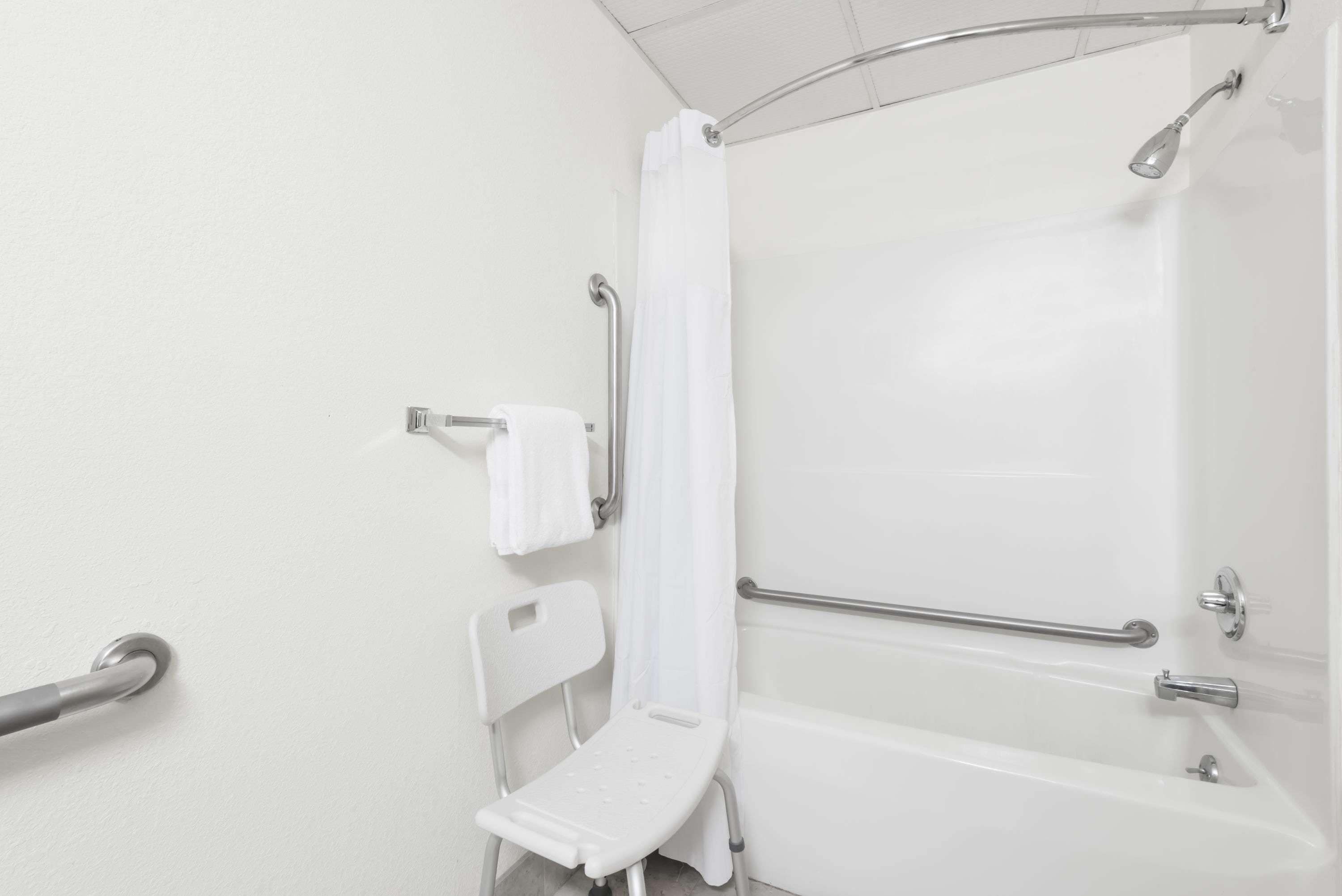 A modern bathroom with a shower, grab bars, and a white chair.