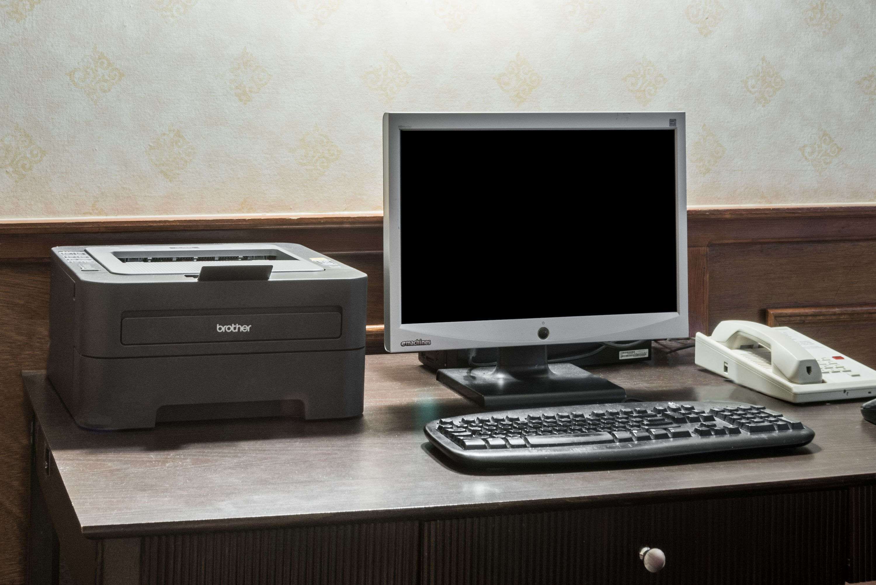 A desk with a Brother printer, an Emachines monitor, a keyboard, and a telephone.
