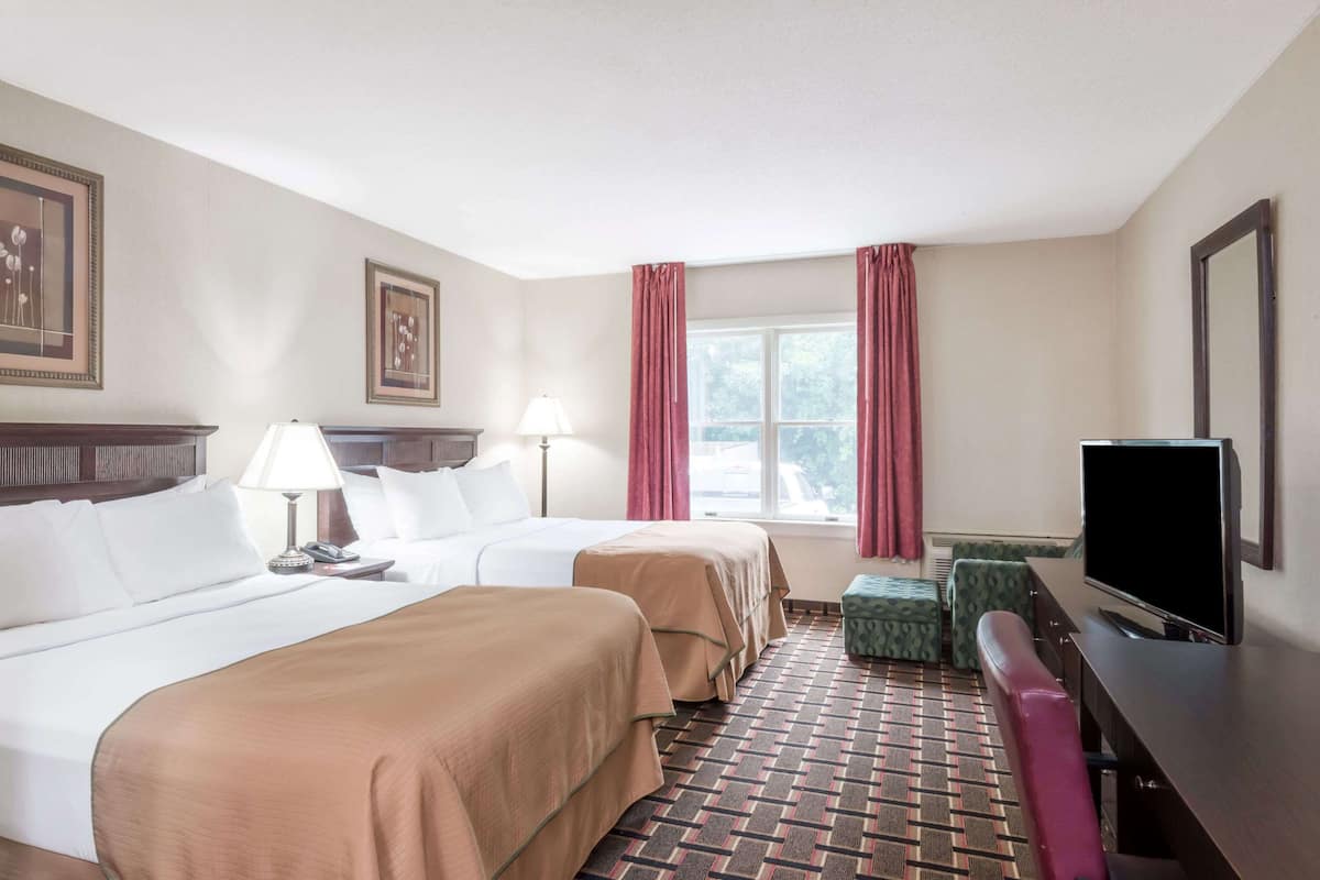 A hotel room with two beds, a television, a desk, and a window with curtains.