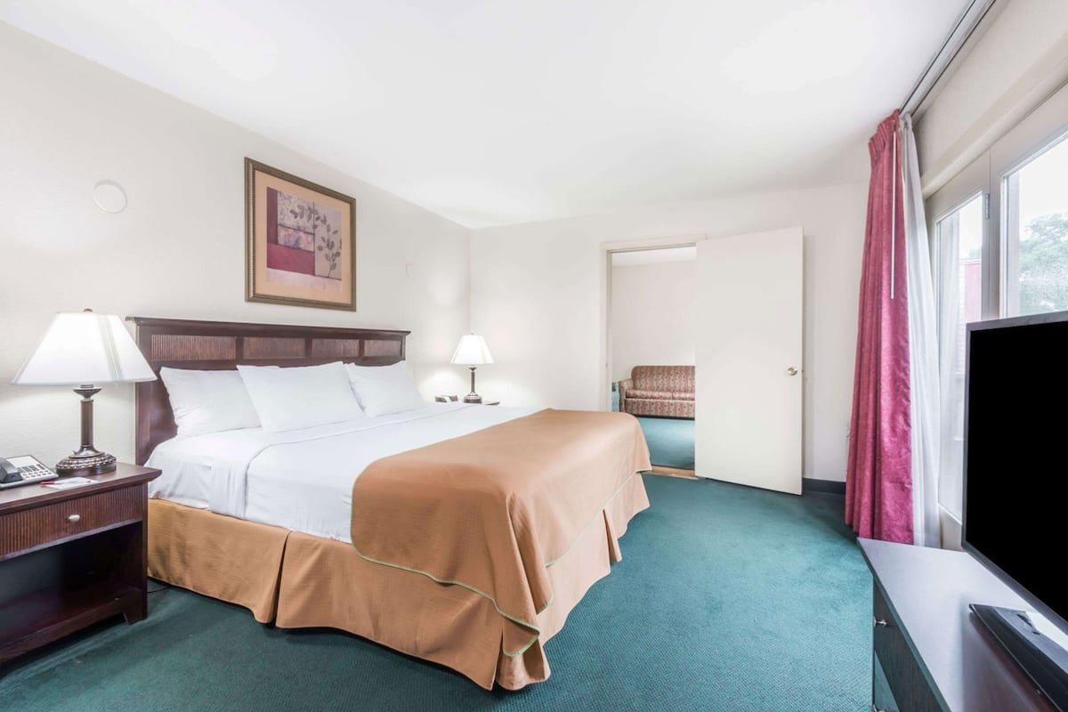 A hotel room with a bed, bedside tables, a television, a chair, and a door leading to another room.