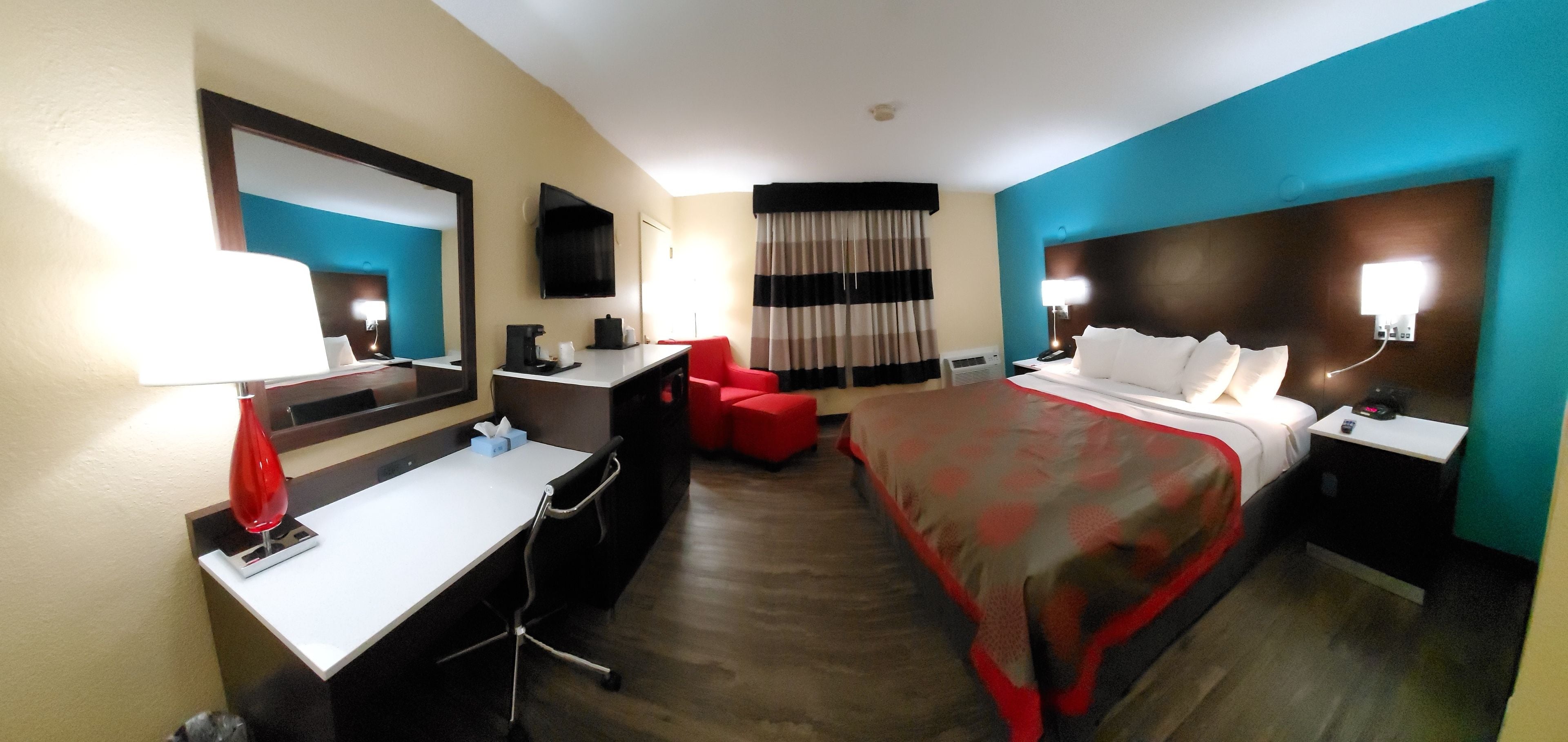 A hotel room with a bed, desk, chair, and a large mirror.