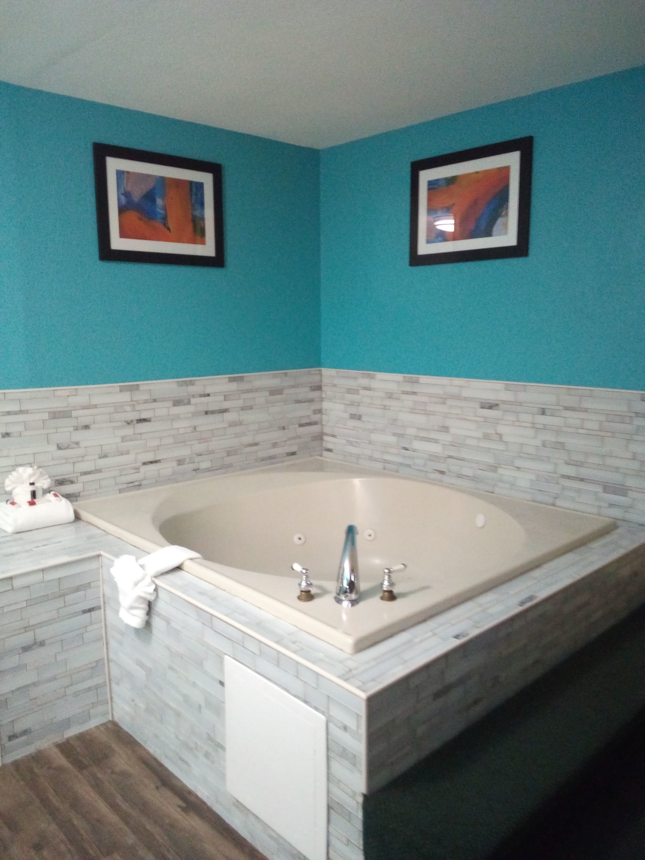 A bathroom with a large bathtub, a white towel rack, and two framed artworks on the turquoise walls.