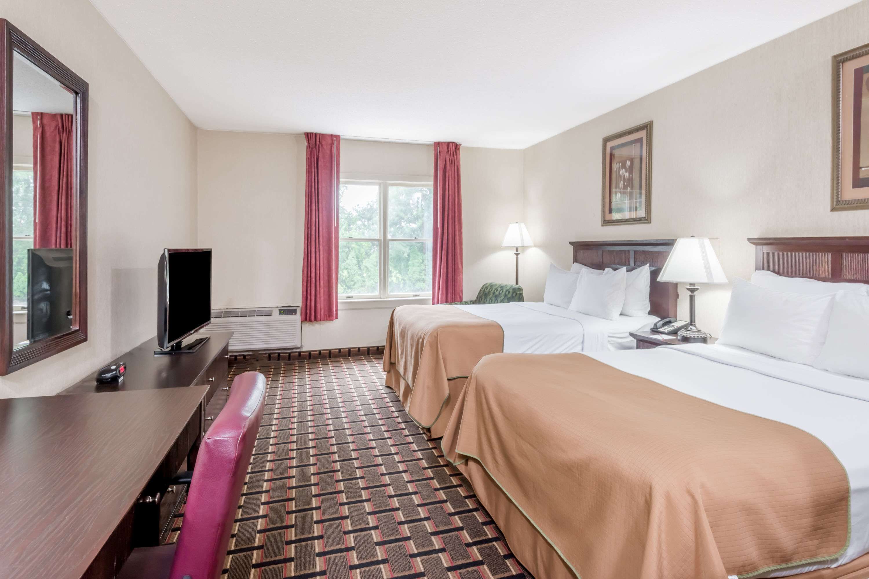 A hotel room with two beds, a desk, a television, and a window with curtains.