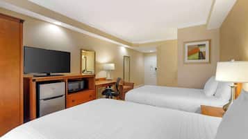 Habitación de hotel con dos camas, un escritorio con computadora, televisión, refrigerador, una silla y una lámpara.