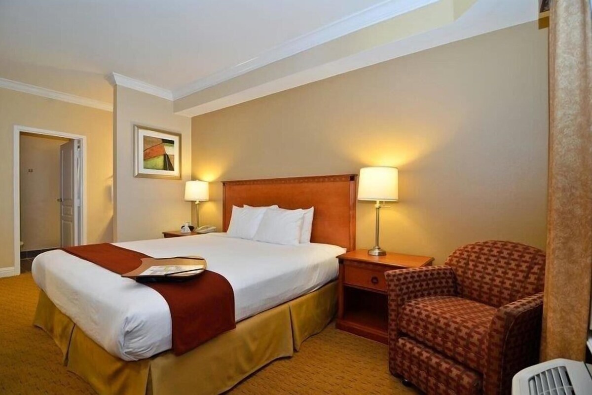 Una habitación de hotel con una cama, lámparas de noche, un sillón y una puerta.