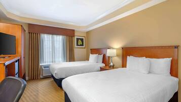 A hotel room with two beds, a desk with a TV, a chair, and a window with curtains.