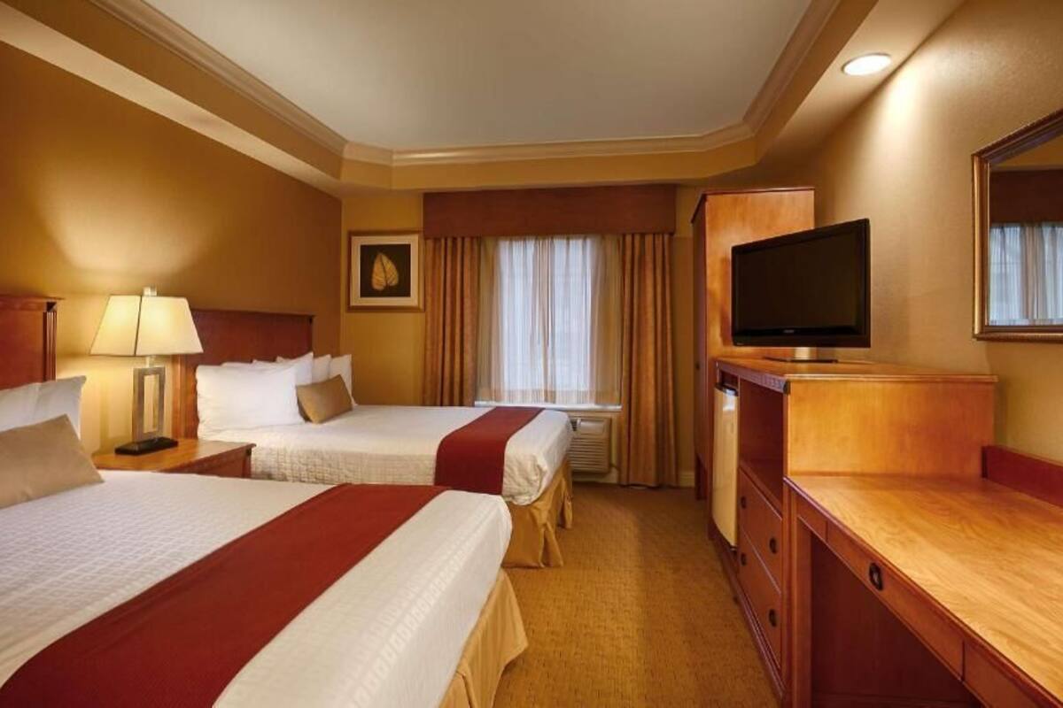 Una habitación de hotel con dos camas, televisión, escritorio y un espejo grande.