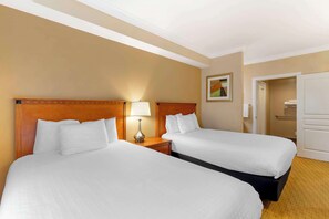A hotel room with two beds, a nightstand with a lamp, a painting on the wall, and a door leading to a bathroom. - Best Western Plus Kingsland (Kingsland)