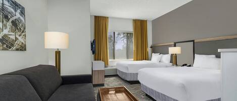 Une chambre d’hôtel avec un canapé, deux lits, un ventilateur de plafond, une lampe et une petite table d’appoint.