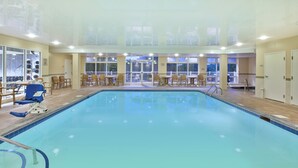 Una piscina interior con vista despejada al área de la piscina, un área de descanso con sillas y mesas, y un balcón con barandilla.