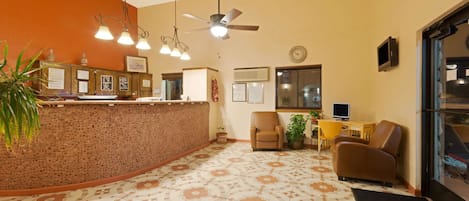 A hotel lobby with a reception desk, seating area, and a ceiling fan.